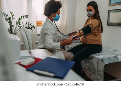 Eine schwangere Frau während einer routinemäßigen Kontrolle bei ihrem Arzt. Ärztin misst Druck auf sie, während sie Gesichtsmasken trägt
