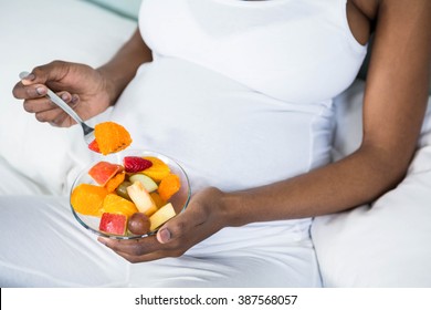Pregnant woman eating fruit salad lying on her bed