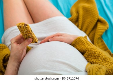 Pregnant Woman Eating Granola Bar. Aerial Close Up View.