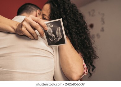 Pregnant Woman Embracing Future Baby’s Father Holding Printed Ultrasound. Young pregnant girl hugging partner holding baby’s ultrasound print. - Powered by Shutterstock