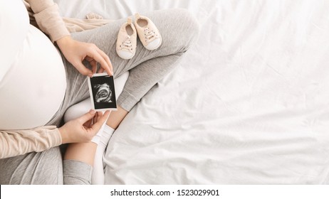 Pregnant Woman Enjoying Future Motherhood With First Ultrasound Photo Of Her Baby, Top View With Free Space