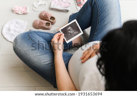 Pregnant woman enjoying future motherhood with her baby's first ultrasound photo, top view with free space