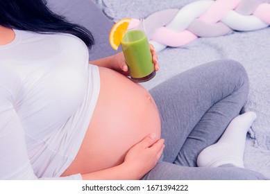 Pregnant woman enjoying her healthy organic green juice while relaxing on the couch at home. 