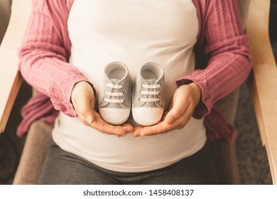 Pregnant Woman Feeling Happy At Home While Taking Care Of Her Child. The Young Expecting Mother Holding Baby In Pregnant Belly. Maternity Prenatal Care And Woman Pregnancy Concept.