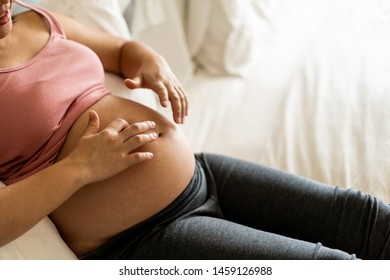 Pregnant woman feeling happy at home while taking care of her child. The young expecting mother holding baby in pregnant belly. Maternity prenatal care and woman pregnancy concept. - Shutterstock ID 1459126988