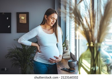 Pregnant woman feels stomach pain, tries to relax by the window, suffers from abdominal pain, pregnant woman has cramps, copy space - Powered by Shutterstock