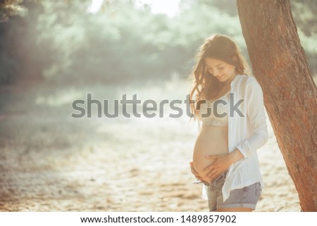 Pregnant woman at the forest next to the tree.