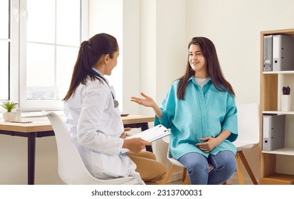 Pregnant woman gets professional consultation at prenatal clinic. Happy young woman and her OB GYN obstetrician gynecologist doctor sitting in medical office and talking. Pregnancy, healthcare concept - Powered by Shutterstock