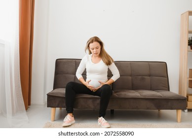 Pregnant Woman Getting Up From Sofa With Hand On Hip At Home