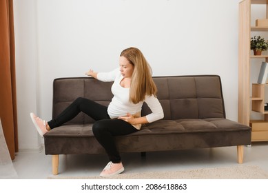 Pregnant Woman Getting Up From Sofa With Hand On Hip At Home