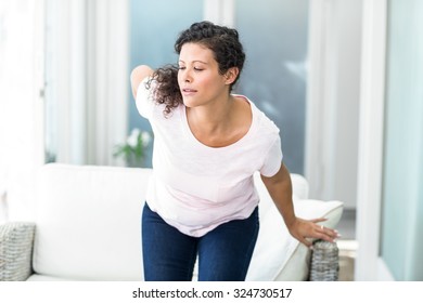 Pregnant Woman Getting Up From Sofa With Hand On Hip At Home