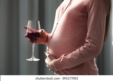 Pregnant woman with glass of red wine in hand indoors
