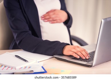 A pregnant woman hand on belly closeup uses laptop in the office