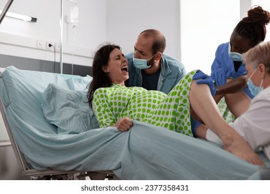 Pregnant woman having caesarean surgery, pushing hard while medical team delivery baby in hopsital ward. Pregnant woman having paniful contractions giving birth to child, being comforting by husband - Powered by Shutterstock