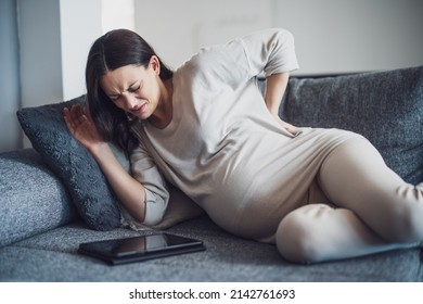 Pregnant Woman Is Having Pain In Her Back. She Is Lying On Bed At Home.