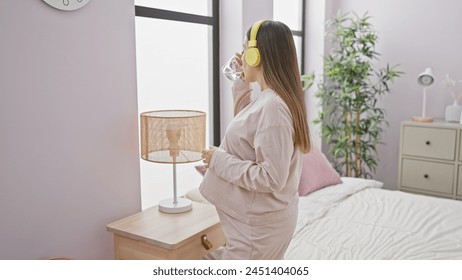 A pregnant woman with headphones drinking water in a modern bedroom. - Powered by Shutterstock