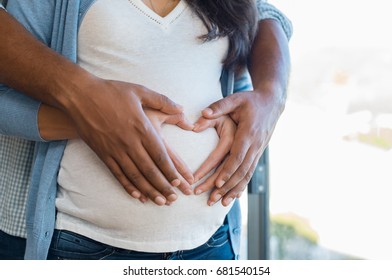 Pregnant woman and her african husband holding hand in heart shape on baby bump. Close up of multiethnic couple making heart shape on the tummy. Loving future couple expecting a baby. - Powered by Shutterstock