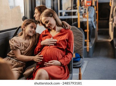 Pregnant woman and her daughter smiling and enjoying together a bus ride with many passengers. - Powered by Shutterstock