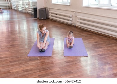 Pregnant woman with her first kid daughter doing gymnastics in living room. 