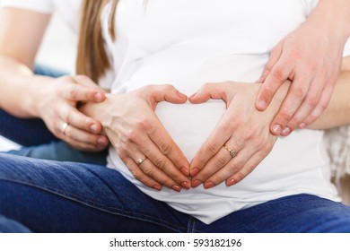 Pregnant Woman and Her Husband holding her hands in a heart shape on her baby bump. parents hands on her stomach Pregnant White T-shirt