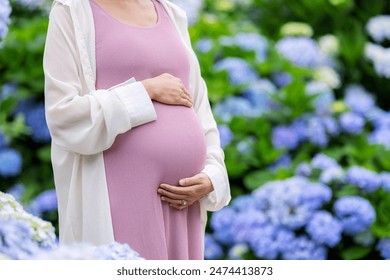 Pregnant woman hold with her tummy at Hydrangea flower garden - Powered by Shutterstock