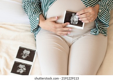 Pregnant Woman Hold Ultrasound 3d Picture Scan Of Unborn Yet Fetus.female Lies In Bed Look Analise Admire Baby Photos Or Sits On Knees On Bed.bedroom Interior.woman Hand On Belly.last Third Trimester