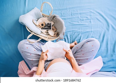 Pregnant woman holding baby bodysuit preparing to child birth during pregnancy. Mother with wicker basket with stuff for baby and ultrasound image. Concept local eco children products, baby shower. - Powered by Shutterstock