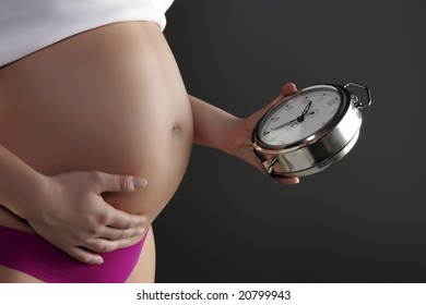 Pregnant woman holding a clock at her belly - Powered by Shutterstock