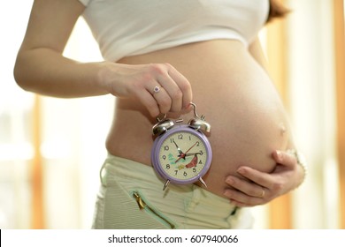 Pregnant woman holding a clock at her belly. - Powered by Shutterstock