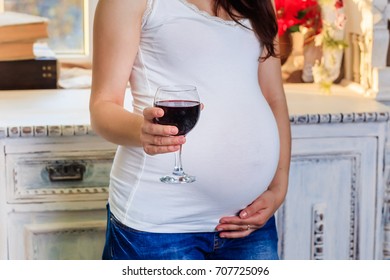Pregnant woman holding a glass of red wine in her hand