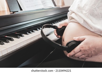 Pregnant woman holding headphones on her belly. Music for the unborn baby's brain and fetal hearing development. Healthy pregnancy and happy baby. Piano background. Soft tone picture. Selective focus.