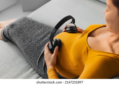 Pregnant Woman Holding Headphones On Belly Listening To Music For Unborn Baby Brain Development. Foetus Can Hear Through The Womb