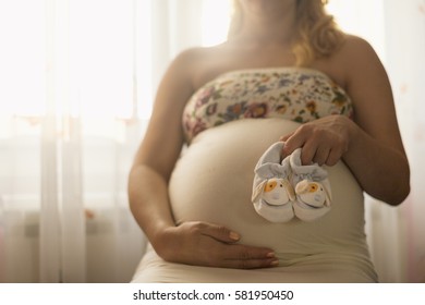 Pregnant woman holding her belly  and showing baby shoes