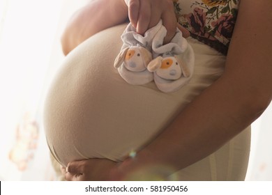 Pregnant woman holding her belly  and showing baby shoes