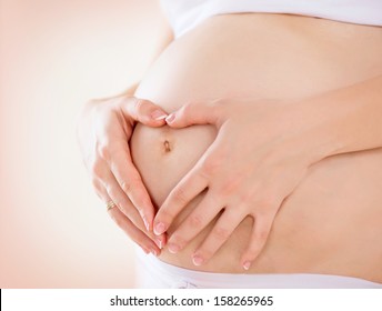 Pregnant Woman holding her hands in a heart shape on her baby bump. Pregnant Belly with fingers Heart symbol. Maternity concept. Baby Shower 
