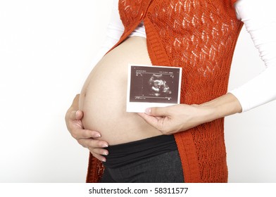 A pregnant woman is holding her stomach and a photo of her Ultrasound. Perfect photo for a love, motherhood, or a trimester concept.