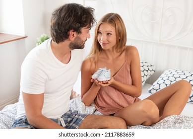 Pregnant woman is holding a little shoes for baby. Happy young couple