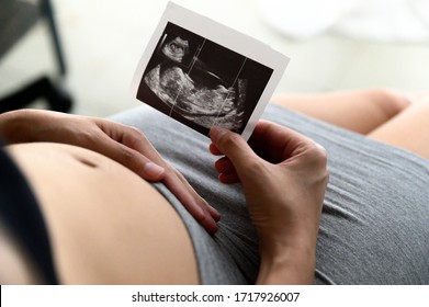 Pregnant woman holding and looking sonogram or ultrasonography picture of her unborn baby