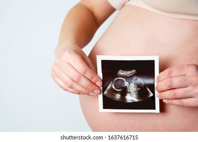 Pregnant woman holding a photo of her ultrasound baby scan. Pregnant belly.