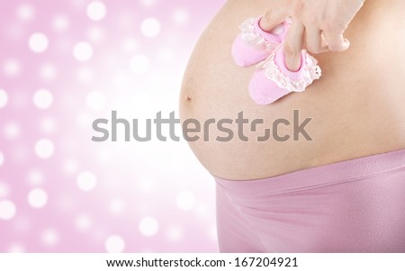 Pregnant woman holding pink baby booties...