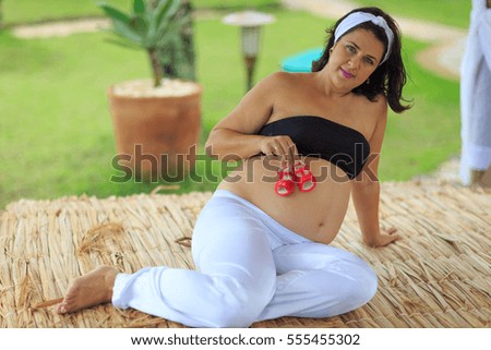 Pregnant woman holding red baby shoes on her belly 