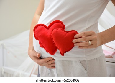 Pregnant woman holding a red heart sign. Pregnant woman put twins toy heart to her stomach on white background