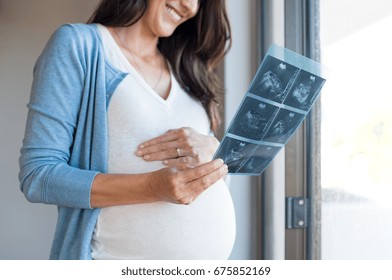 Pregnant woman holding ultrasound report at home. Mature lovely pregnant woman looking at sonogram image of her baby. Close up hands of woman looking at baby in ultrasound image x ray.