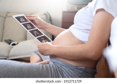 Pregnant woman holding ultrasound scan photo on her belly at home. Mother with sonogram of her unborn baby. Concept of pregnancy, Maternity prenatal care