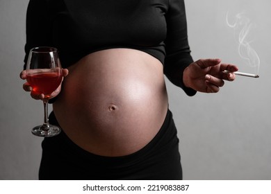 A Pregnant Woman Is Holding Wine In Her Hands And Smoking A Cigarette. The Concept Of Harm Of Smoking And Alcohol Consumption During Pregnancy. High Quality Photo