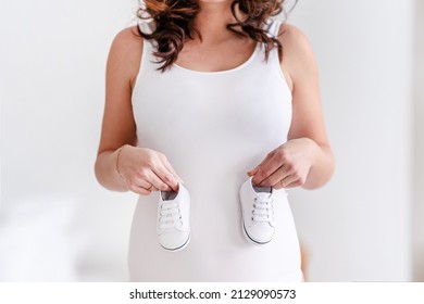A pregnant woman holds the baby's shoes on her big belly. Beautiful healthy pregnancy, waiting for the birth of a baby