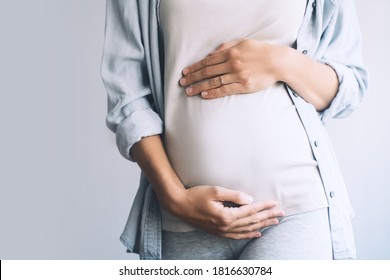 Pregnant woman holds hands on belly on white background. Mother waiting for baby birth. Women prepare for maternity. Concept of pregnancy, gynecology, prenatal period, maternal health.