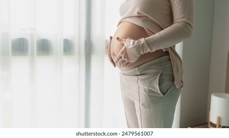 Pregnant woman holds hands on belly touching her baby caring about her health - Powered by Shutterstock