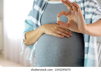 Pregnant woman at home hold pill in hand. Baby expectation, health care and prenatal vitamins on pregnancy time. Illness and medicine while pregnancy. - Shutterstock ID 2192295073