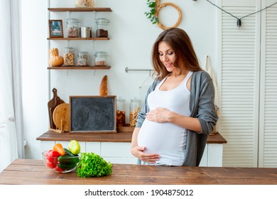 Pregnant Woman At Home In The Kitchen Eating Vegetables